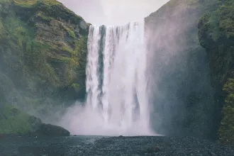 Powerful waterfall cascading down a moss-covered cliff into a misty pool below