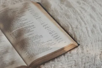 Open Bible resting on a soft white blanket with gentle light falling across the pages