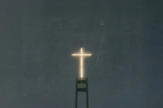 Illuminated cross glowing atop a tall church structure against a dark night sky