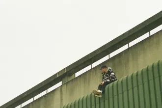 Silhouetted figure standing at the top of a walkway lined with tall flagpoles under a hazy evening sky