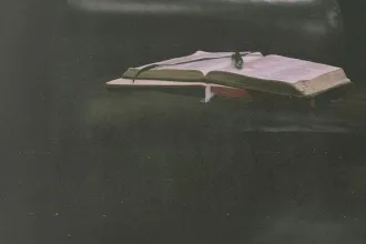 Open Bible resting on a dark leather surface with a ribbon marker and soft, moody lighting