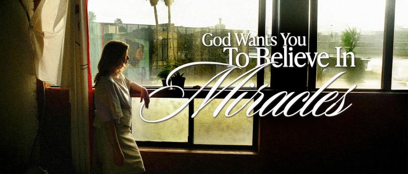 Person standing by a sunlit window with plants, gazing outside as Miracles feel possible in a calm urban setting.