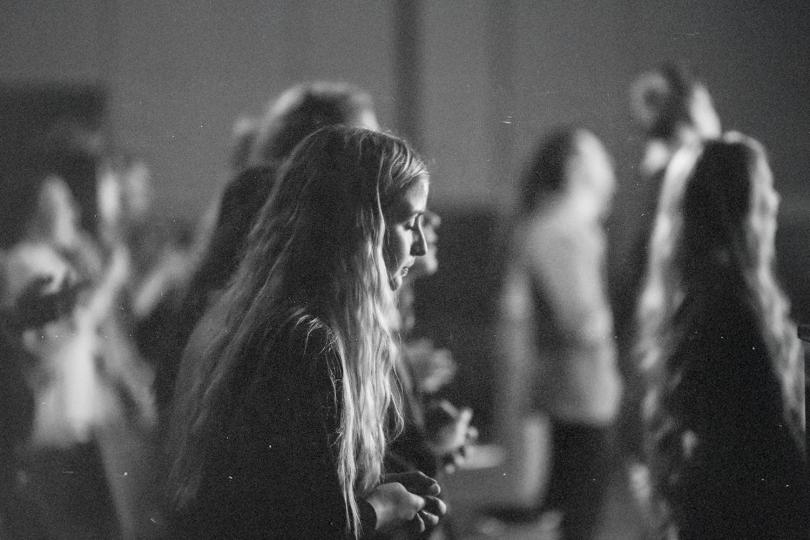 Group of people standing closely together in a dimly lit indoor setting during worship.