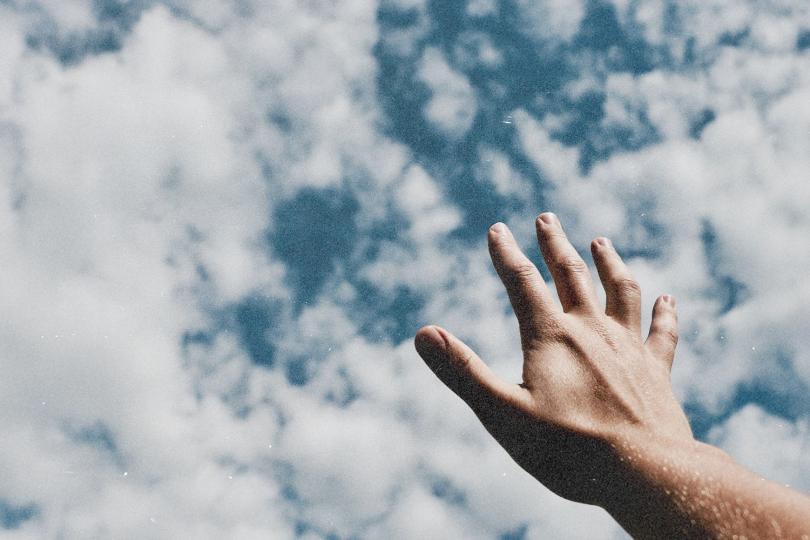 Hand extended upward toward a sky filled with scattered white clouds