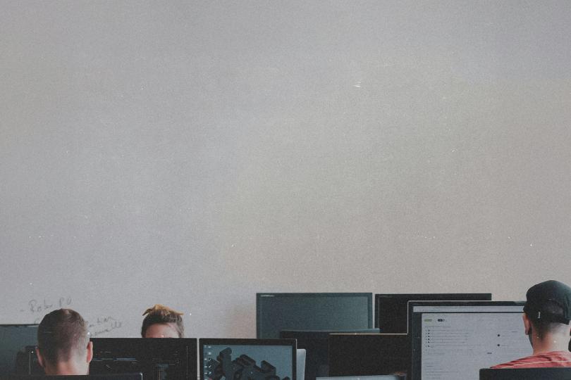 People seated at computer stations in a classroom with multiple monitors facing the front of the room