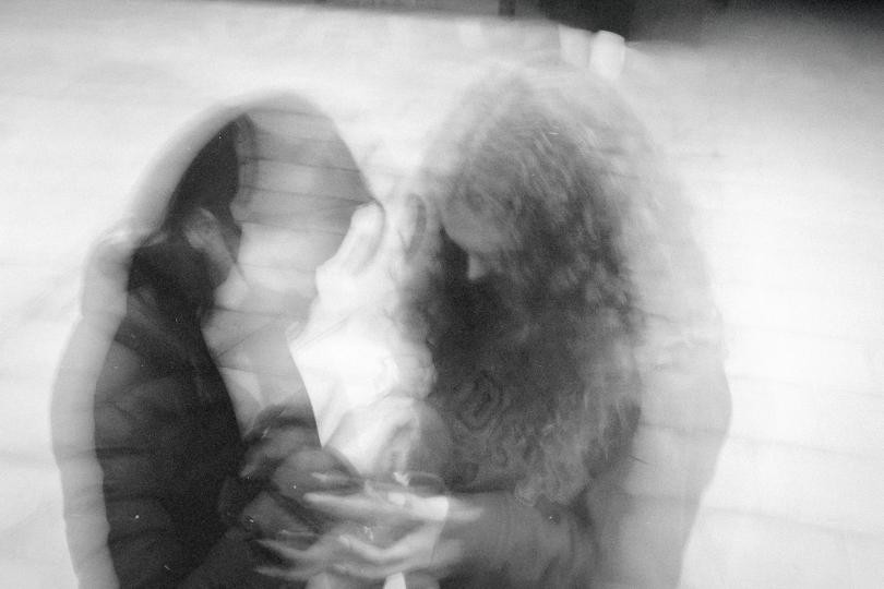Two people sitting closely together in a soft, double‑exposed black‑and‑white image, creating a dreamy, motion‑blur effect