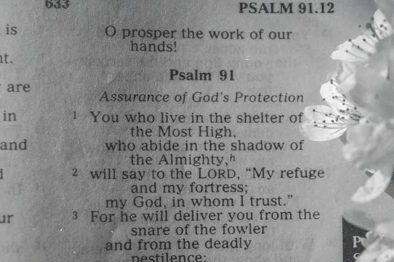 Open Bible displaying Psalm 91 with delicate white flowers resting beside the page