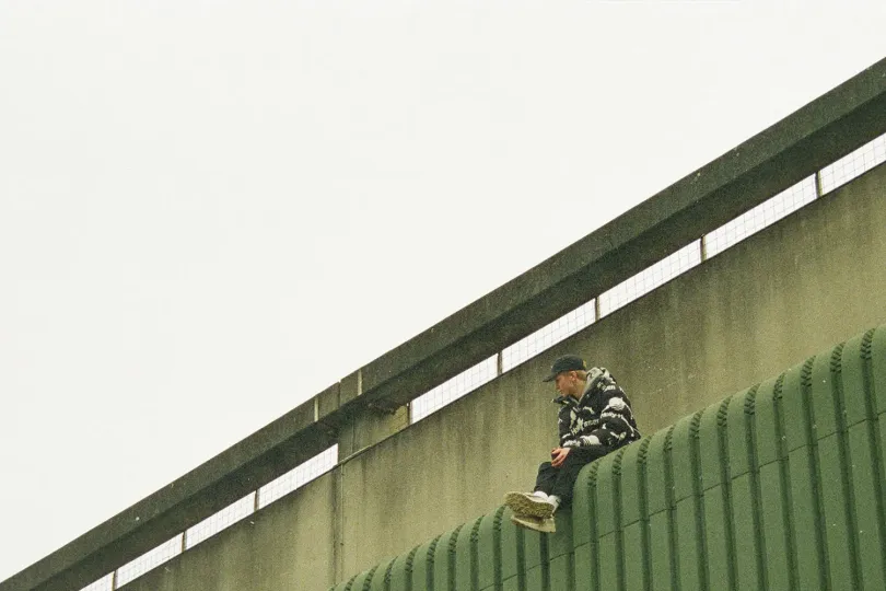 Silhouetted figure standing at the top of a walkway lined with tall flagpoles under a hazy evening sky
