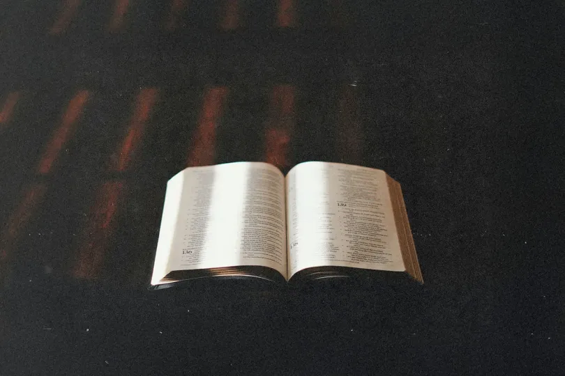 Open Bible illuminated by soft light on a dark wooden surface